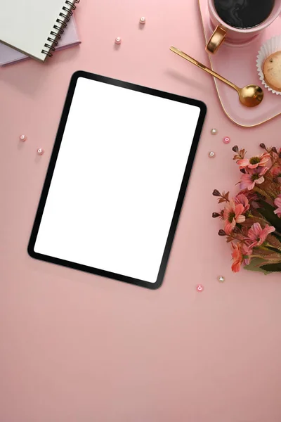 Digital tablet with blank screen, coffee cup, notebook and red flower on pink background.