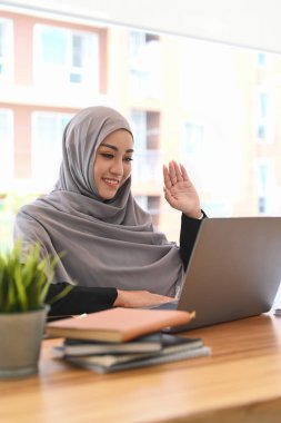 Happy young Muslim woman communicating by video conference on laptop computer.