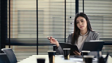 Dijital tablet kullanan çekici bir iş kadını, yanında istatistik belgeleriyle parlak ofisinde oturuyor..