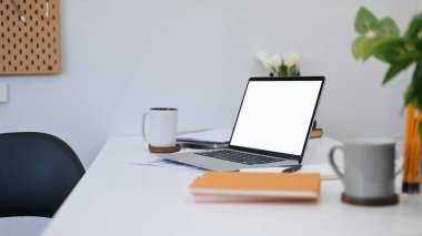 Computer laptop with blank screen, coffee cups, notebook and houseplant on white table.