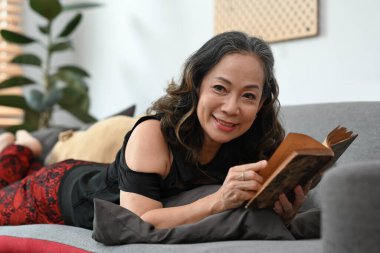 Mutlu orta yaşlı kadın rahat koltukta uzanıp ilginç kitaplar okuyor..