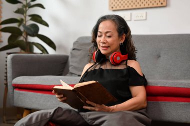 Huzurlu orta yaşlı kadın en sevdiği romanı okuyor, oturma odasında rahat bir şekilde yerde oturuyor..