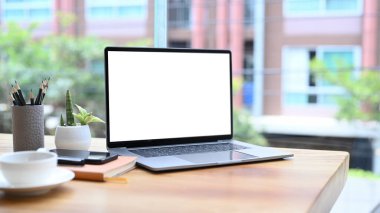 Laptop bilgisayarı, kahve fincanı, kalem tutacağı ve sulu bitkisi olan ahşap ofis masası..