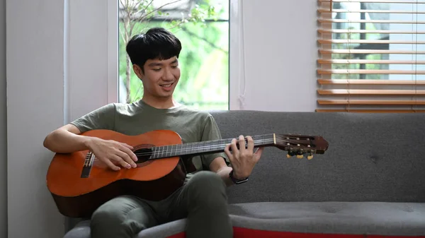 Happy Asian Man Playing Acoustic Guitar Couch Enjoying Carefree Time — Fotografia de Stock