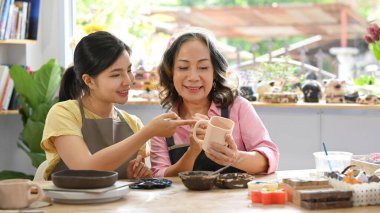 Olgun bir kadın, atölyede esrar yontan genç bir kadına ders veriyor..