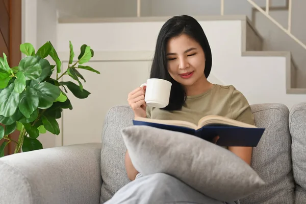 Young Woman Drinking Hot Tea Reading Interesting Book Couch Home — 스톡 사진