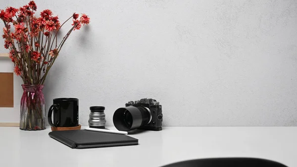 Freelancer workplace with camera, notebook, picture frame and flower pot on white table.
