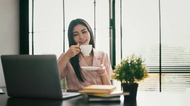 Kahve içen, internet haberlerini ya da iş e-postalarını bilgisayarında okuyan mutlu bir çalışan kadın..