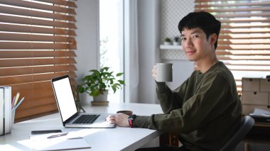 Gülümseyen Asyalı genç adam internette geziniyor, dizüstü bilgisayarda çalışıyor..