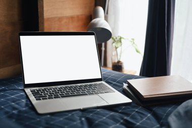 Laptop with blank screen and notebooks in cozy bedroom.