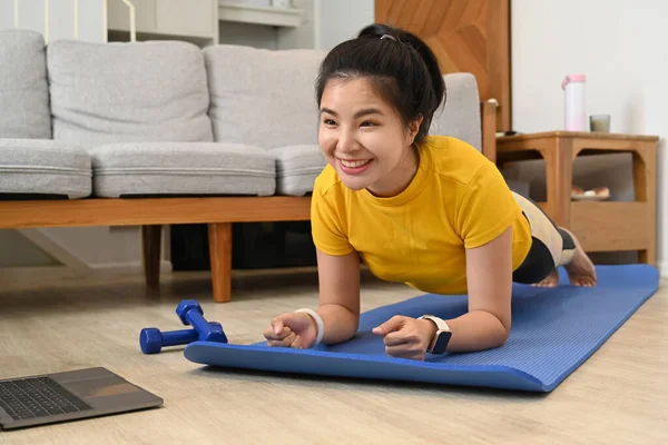 Spor yapan bir kadın apartmandaki spor salonunda spor yaparken dizüstü bilgisayarda ders seyrediyor..