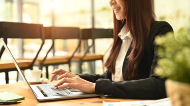 Smiling young employee using laptop, working on research project at coffee shop.