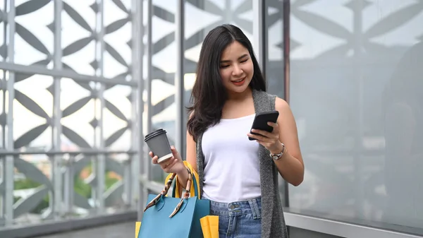 Alışveriş Torbalarıyla Gülümseyen Akıllı Telefon Kullanan Alışveriş Merkezinin Dışında Yürüyen — Stok fotoğraf