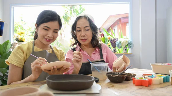 Çömlek atölyesinde çalışmadan önce mutlu bir emekli kadın ve kızı kâseye resim yapıyor..
