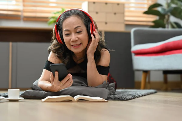 Joyful Middle Aged Woman Wearing Headphone Using Moiled Phone While — 스톡 사진
