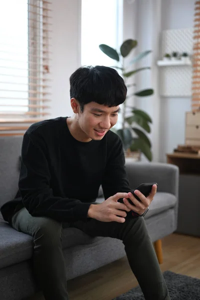 Smiling Young Asian Man Resting Couch Cozy Living Room Using — Φωτογραφία Αρχείου