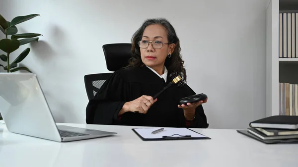 Mature woman in robe gown uniform having video conference, providing law consultation and legal advice online.