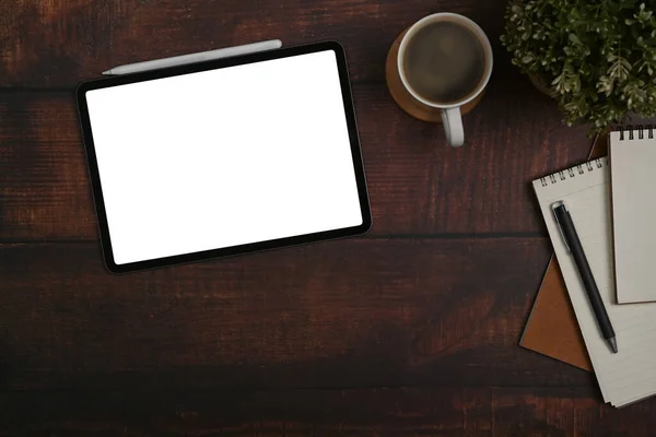 Digital tablet, coffee cup, notebook and potted plant on wooden office desk.