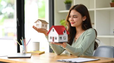 Güzel genç bir kadın ev modelini tutuyor, gayrimenkul yatırımı planlıyor..
