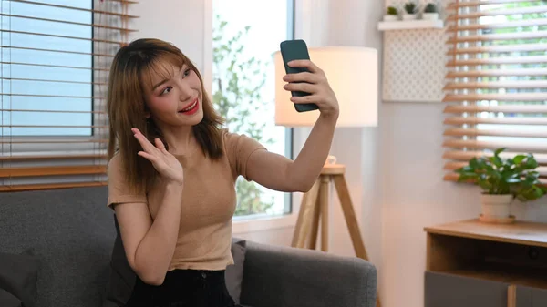 Cheerful young woman waving hand, chatting online, making video call on her smart phone.