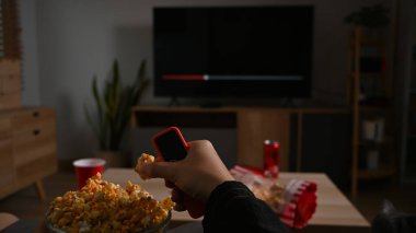 Young man with popcorn and remote control while watching movie in his living room at night.