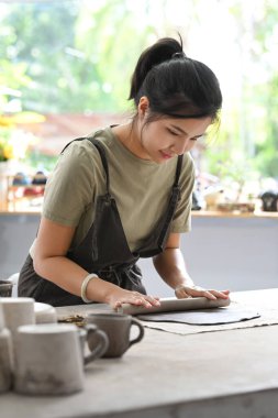 Female potter rolling pin for clay mass, making handicrafts at her studio. Creative hobby, ceramic works concept.