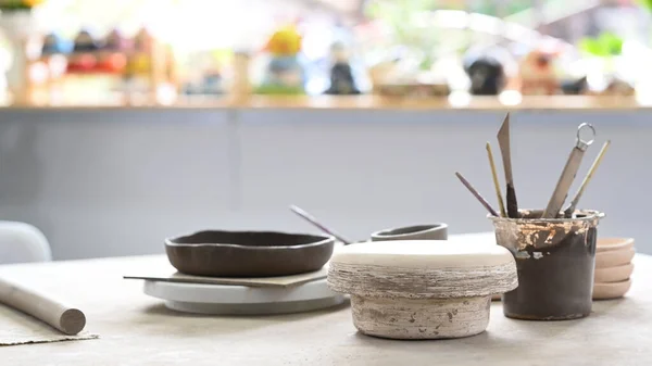 Handmade ceramic dish ware and pottery shaping tools on stone table in creative studio.