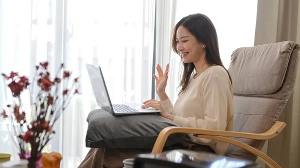 Positive young woman waving hand, chatting online, making video call on her laptop.