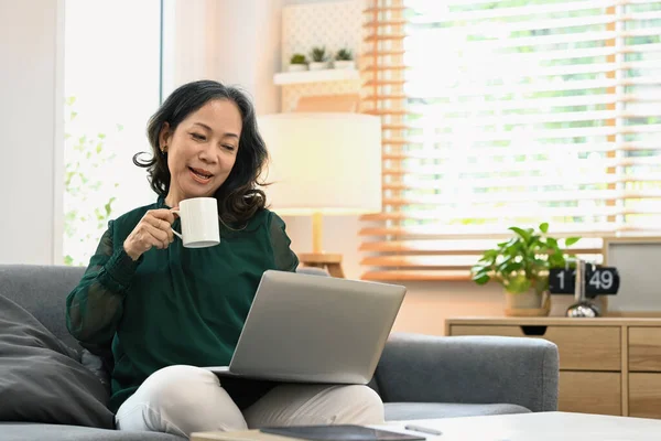 Joyful Middle Aged Woman Casual Clothes Drinking Coffee Using Laptop — Zdjęcie stockowe