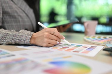 Cropped view of female interior designer working with color swatches at office desk in creative office.