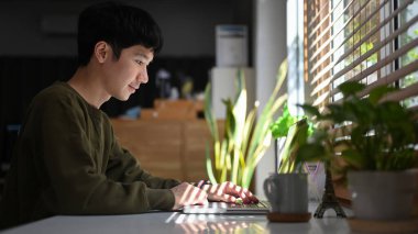 Side view of young man surfing online, checking email on laptop, spending leisure in cozy winter or autumn weekend.