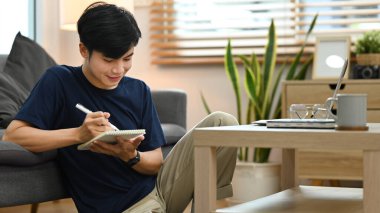 Young asian man making important notes, agenda plan planning daily appointment and write business trip in notebook.