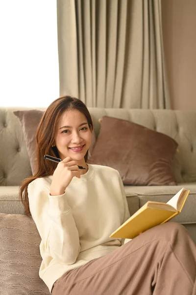 Beautiful young woman with notebook sitting in comfortable home. Leisure activity, positive mood concept.