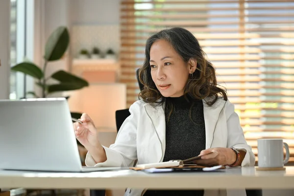 Elegant mature business woman remote working from home, watching online webinar on her laptop computer.