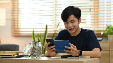 Young man managing household expenses expenditures, paying bills on smart phone.