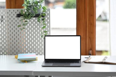 Front view laptop computer with empty screen, notebook and houseplant on white table.
