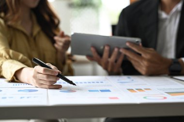 Two business colleges are analyzing investment data on documents at office desk.