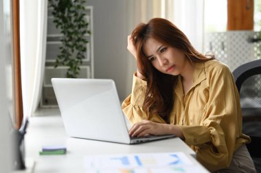 Upset female office worker holding her head on hands while sitting at her workplace. Emotional pressure, stress at work concept.