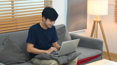 Man in casual clothes sitting on ouch and checking email or working online with laptop.