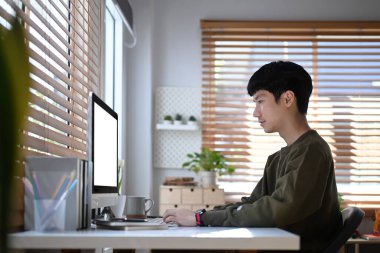 Side view of male freelancer sitting in comfortable home office and working online on computer.