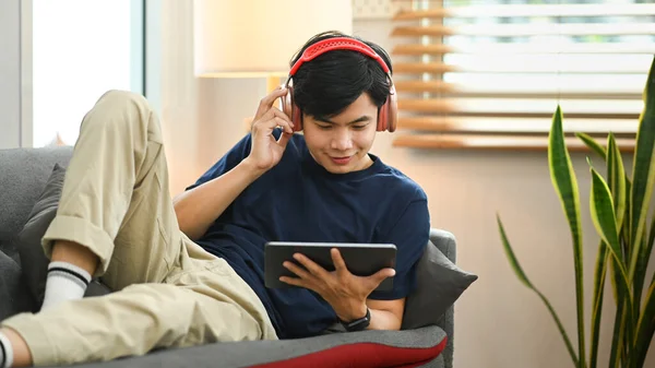 Casual man wearing wireless headphone and watching movie on his digital tablet.