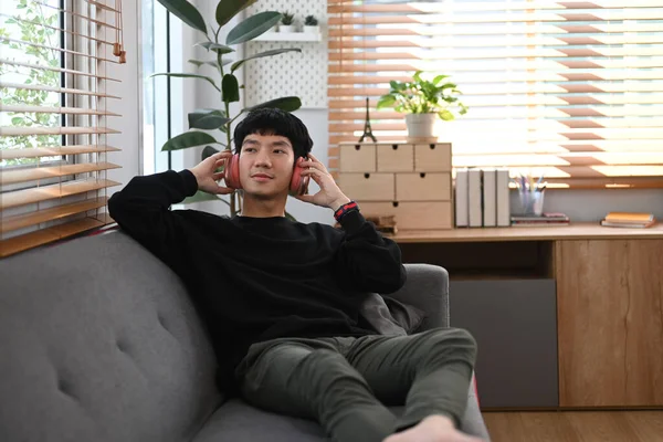 Man wearing warm sweater listening to music on wireless headphones, spending leisure time in cozy winter or autumn weekend at home.
