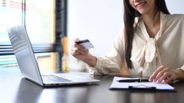 Cropped view of smiling young woman holding credit card and using laptop. Online shopping, e-commerce concept.