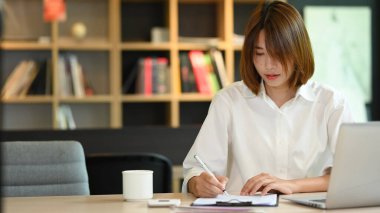 Young businesswoman using laptop and working with financial document at contemporary workplace.