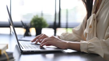 Young businesswoman using laptop and working with financial document at contemporary workplace.