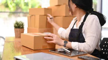 Young asian woman checking product purchase order and preparing parcel for delivery to customers.