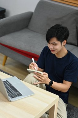 Handsome asian male freelancer working online with laptop and making notes on notepad.