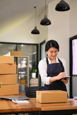 Young business owner preparing parcel boxes of product for delivery to customers at home office. E-commerce, Online selling concept.