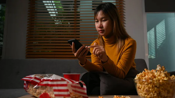 Pretty Young Woman Using Mobile Phone Eating Popcorn Sofa Enjoying — Zdjęcie stockowe
