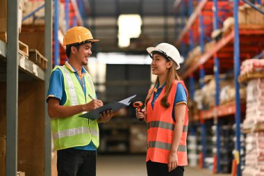 Smiling warehouse workers standing in aisle between rows of tall shelves full of packed boxes. Distribution center and logistic industry concept. 